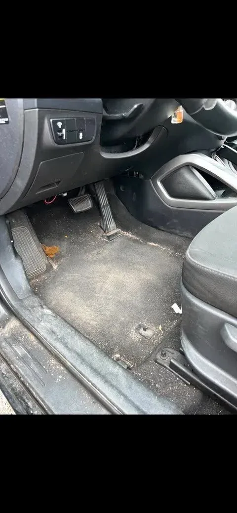 Driver footwell before detailing with dirt and debris on the carpet